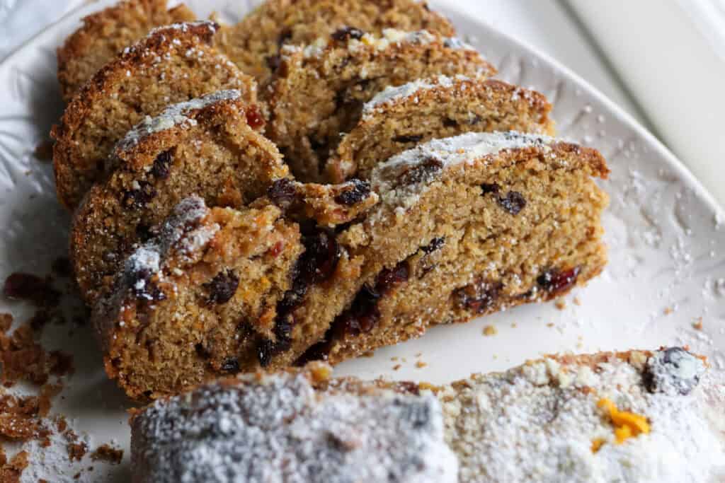 slices of fresh milled Christmas Stollen bread on a white plate with berries and powdered sugar