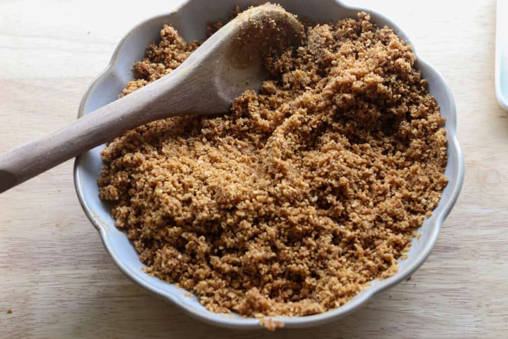 graham cracker crumbs in a bowl to make the crust for No-Bake Mini Christmas Gingerbread Cheesecake Cups