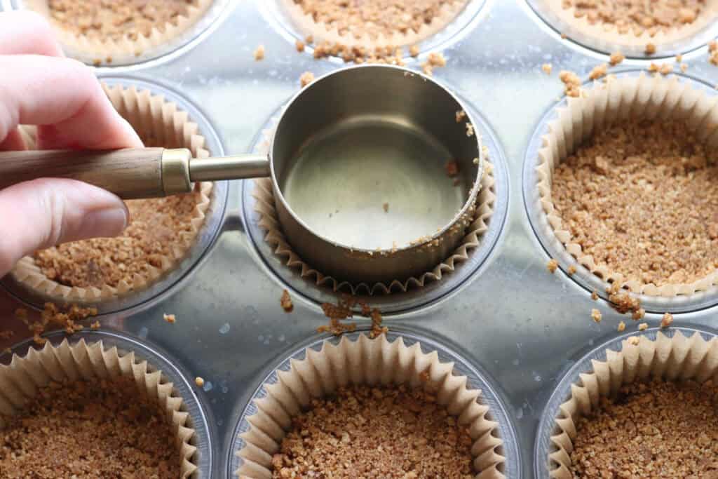 pressing the graham cracker crust into a muffin pan to make No-Bake Mini Christmas Gingerbread Cheesecake Cups