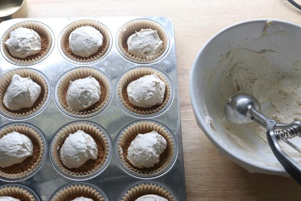 cream cheese filling spooned into a muffin pan to make No-Bake Mini Christmas Gingerbread Cheesecake Cups
