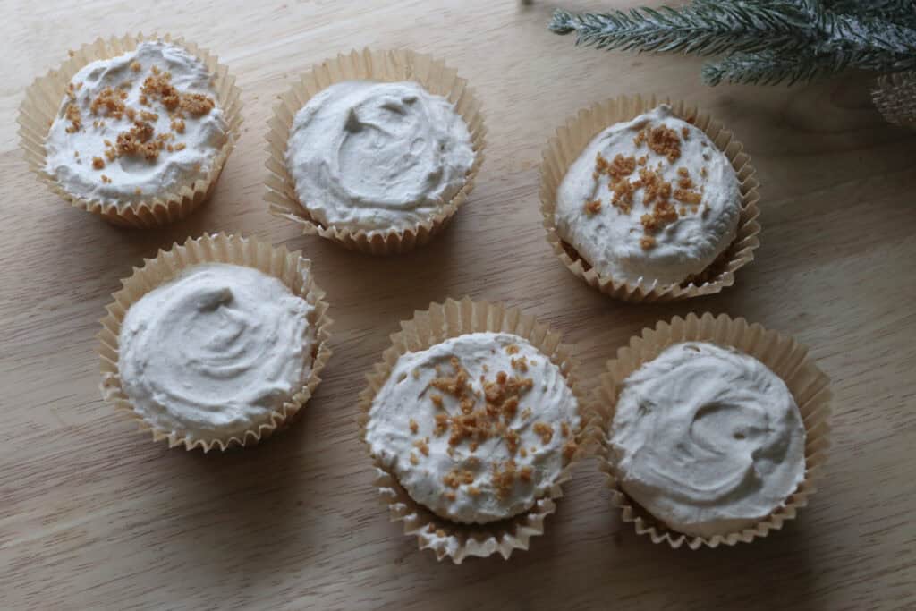 No-Bake Mini Christmas Gingerbread Cheesecake Cups on a wooden board with greenery behind it