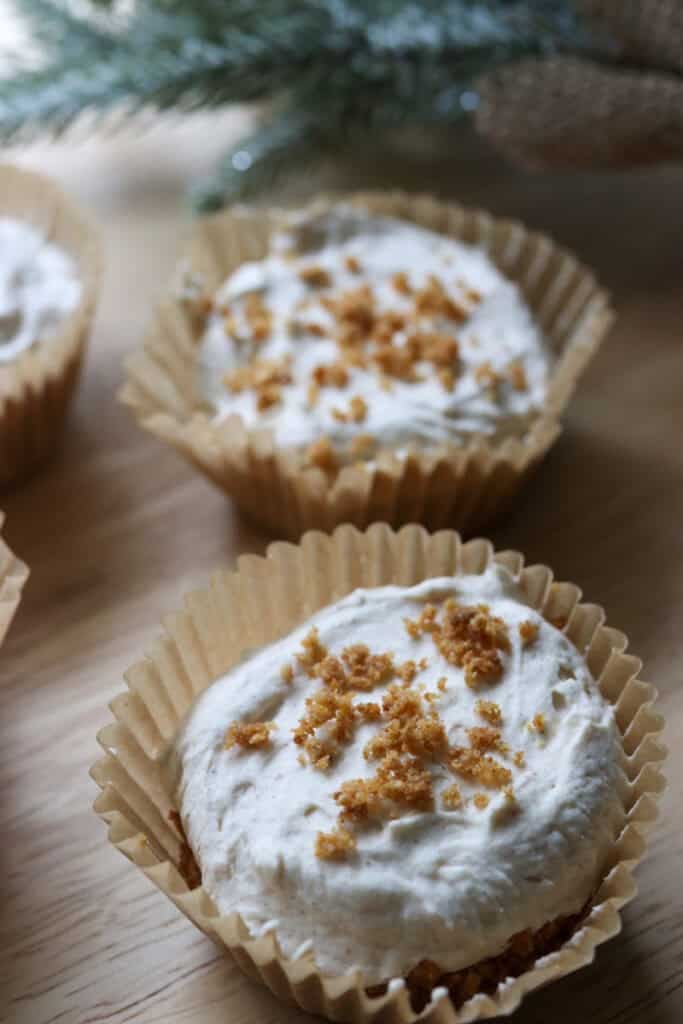 No-Bake Mini Christmas Gingerbread Cheesecake Cups in muffin liners on a wooden board