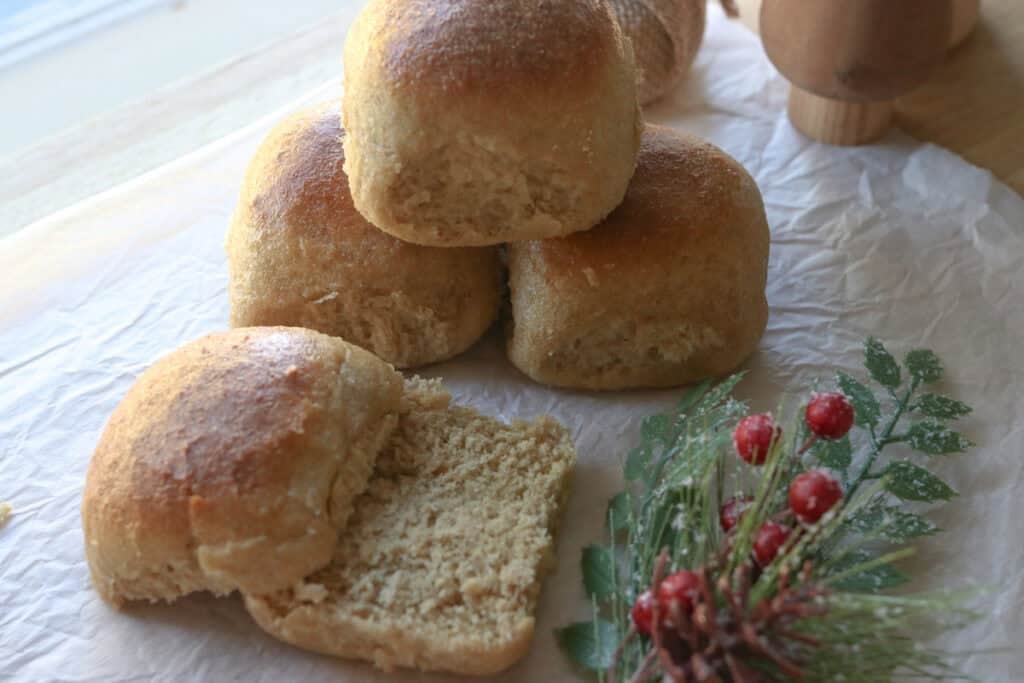 fresh milled fluffy Christmas dinner rolls with one cut in half on parchment paper with greenery