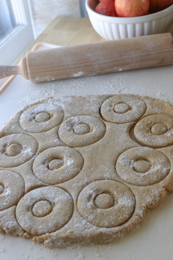 fresh milled apple cider donut dough rolled out with a rolling pin and cut into donut shapes