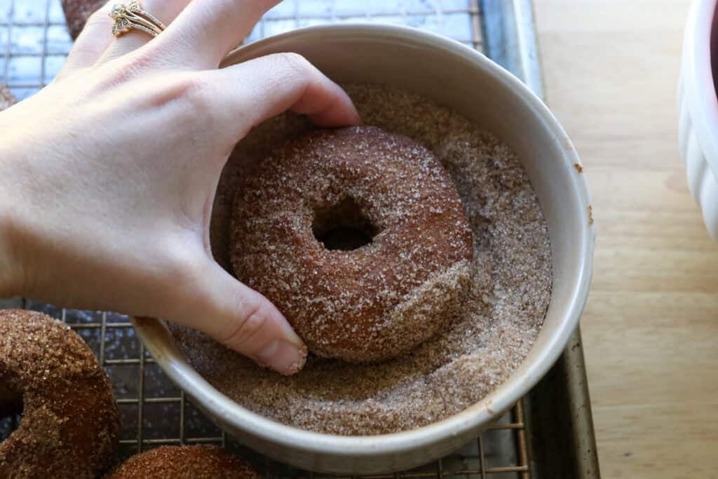 dipping fresh milled apple cider donuts into cinnamon sugar coating