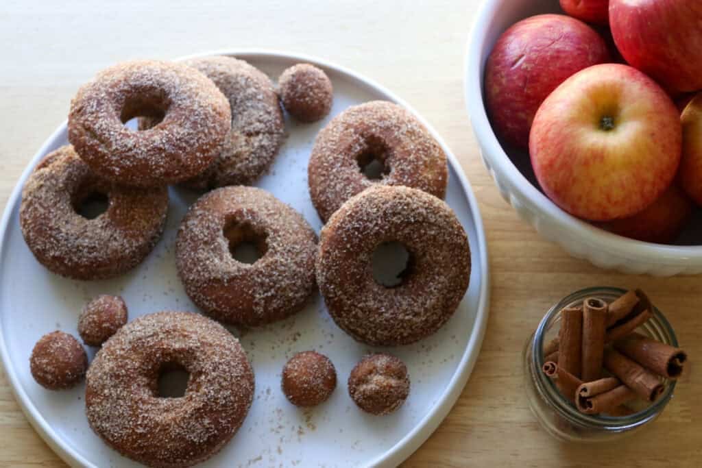 fresh milled apple cider donuts on a white plate covered in cinnamon and sugar