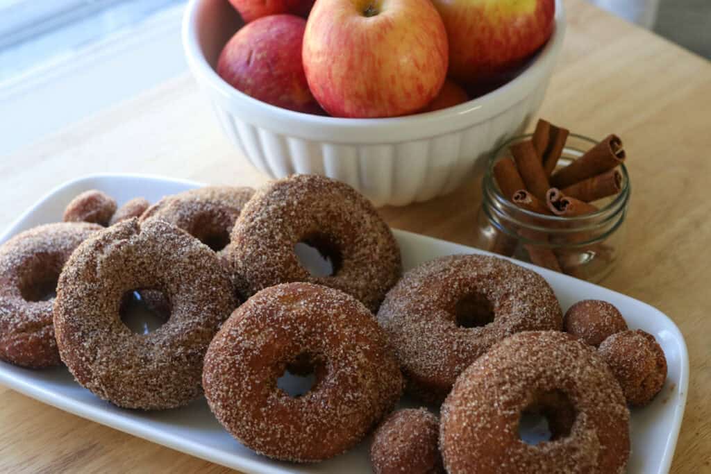 fresh milled apple cider donuts on a white plate with cinnamon sticks