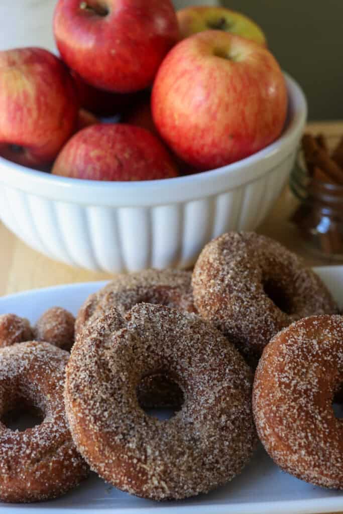 fresh milled apple cider donuts stacked on a white plate that have been dipped in cinnamon and sugar