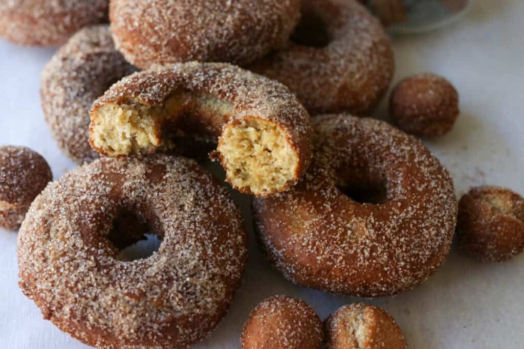 fresh milled apple cider donuts on a white piece of parchment paper with one cut in half
