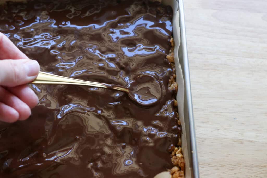 spreading chocolate over top of peanut butter rice krispie bars