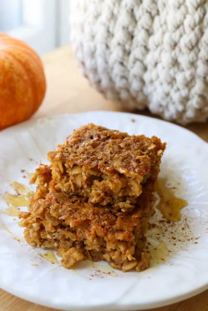 two slices of Healthy High Protein Baked Pumpkin Spice Oatmeal stacked together on a white plate topped with maple syrup