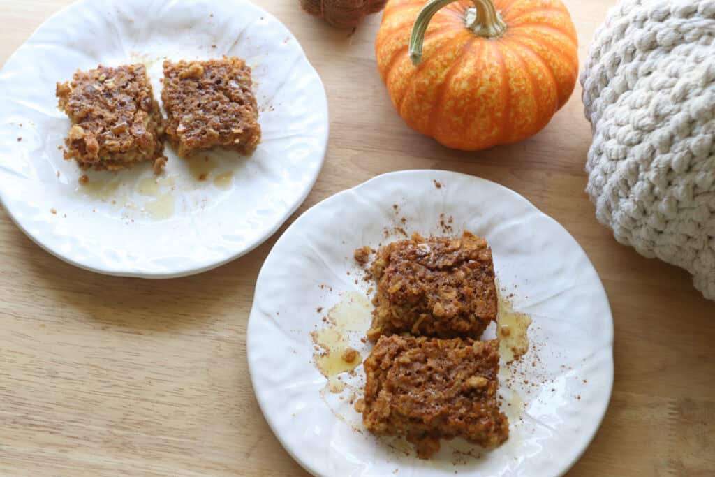 pieces of Healthy High Protein Baked Pumpkin Spice Oatmeal on white plates with a pumpkin