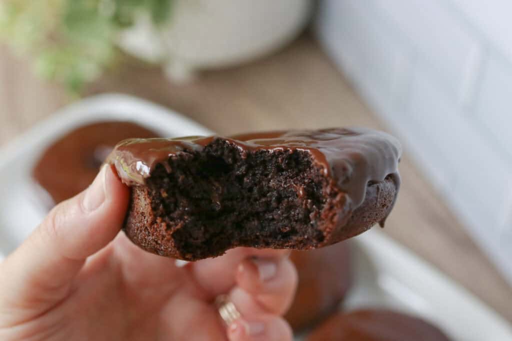 someone holding a Healthy High Protein Chocolate Donut topped with Glaze and a bite taken out of it