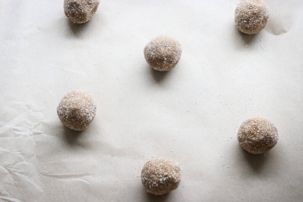 fresh milled gingersnap cookie dough balls that have been rolled in sugar on a baking sheet