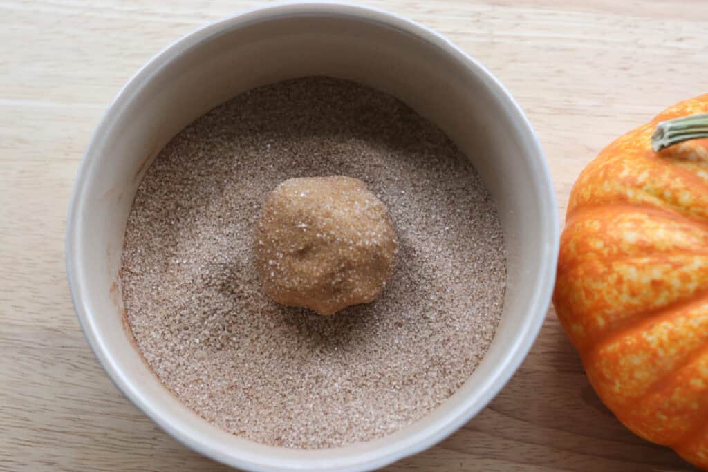 a Freshly Milled Brown Butter Maple Pumpkin Cookie dough ball in a bowl of cinnamon and sugar