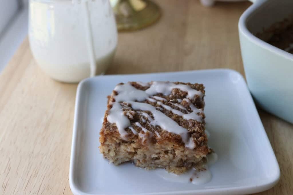 a slice of Healthy Cinnamon Coffee Cake Baked Oatmeal on white plate with glaze on top