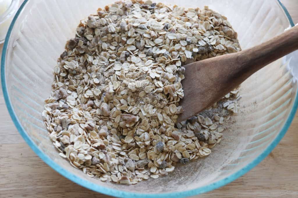 the ingredients to make Healthy and Crunchy Protein-Packed Granola stirred together in a bowl with a wooden spoon