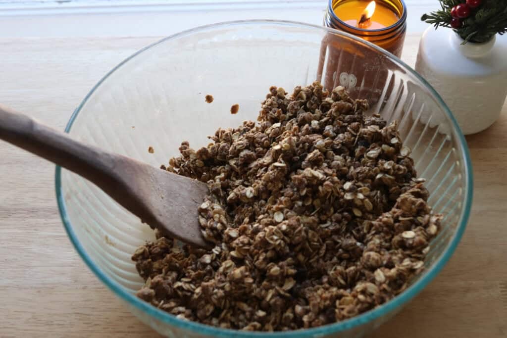 oats, dried fruit, oil, and maple syrup in a glass bowl with a wooden spatula to make Healthy and Crunchy Protein-Packed Granola