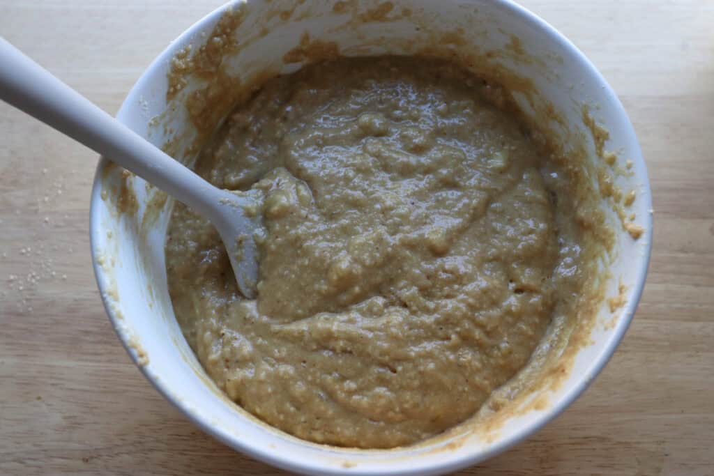 the batter for high protein banana muffins in a white bowl with a spatula