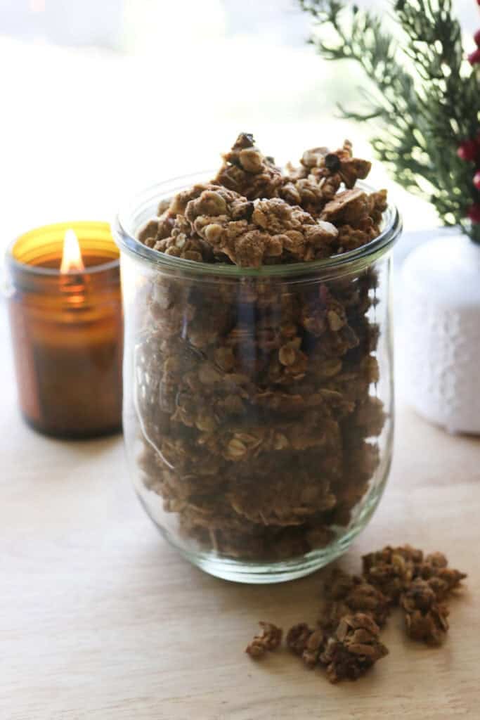 Healthy and Crunchy Protein-Packed Granola in a glass container with granola on the counter and a candle