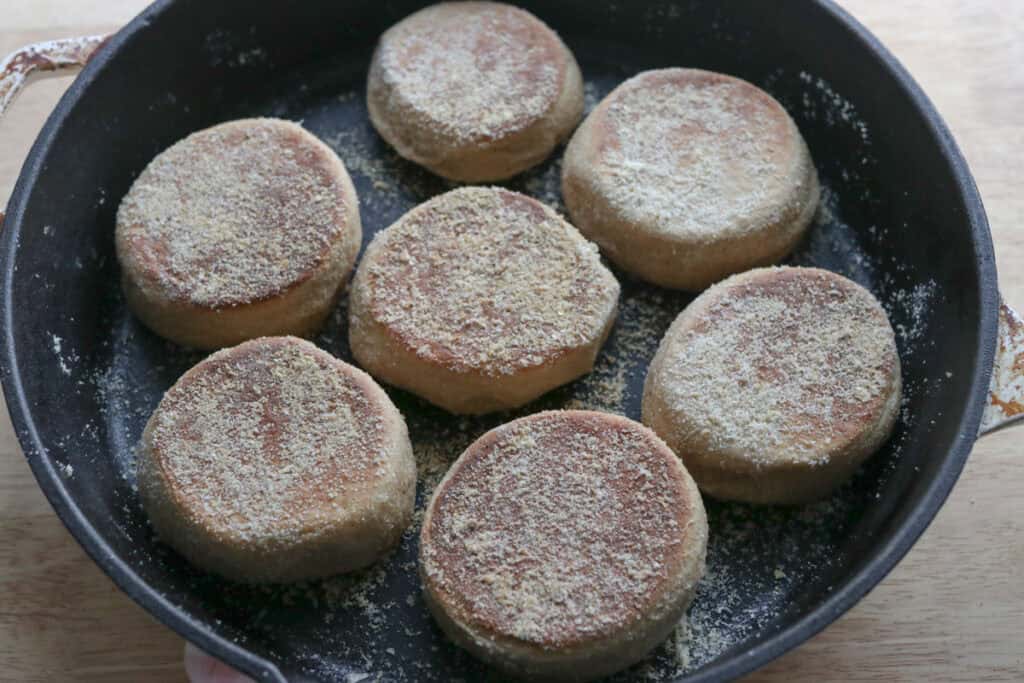 freshly milled english muffins in a cast iron pan that have been cooked