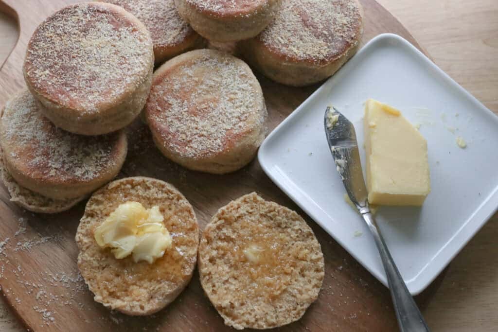 freshly milled english muffins on a cutting board with butter on a white plate