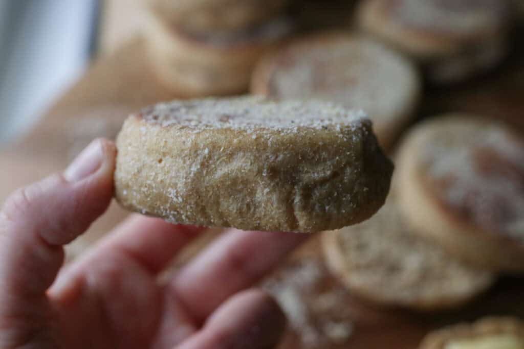 someone holding a freshly milled english muffin with cornmeal on it