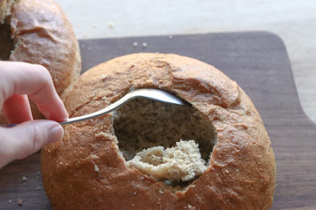 scooping out the inside of a freshly milled soup bread bowl with a spoon