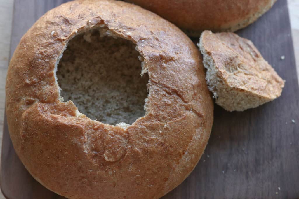 a freshly milled soup bread bowl on a wood cutting board with the top cut out