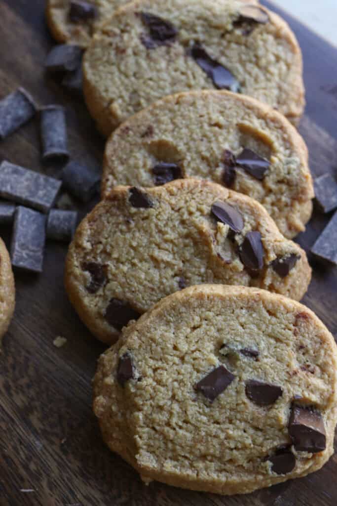 four Freshly Milled Slice and Bake Chocolate Chunk Cookies with chocolate chunks beside it