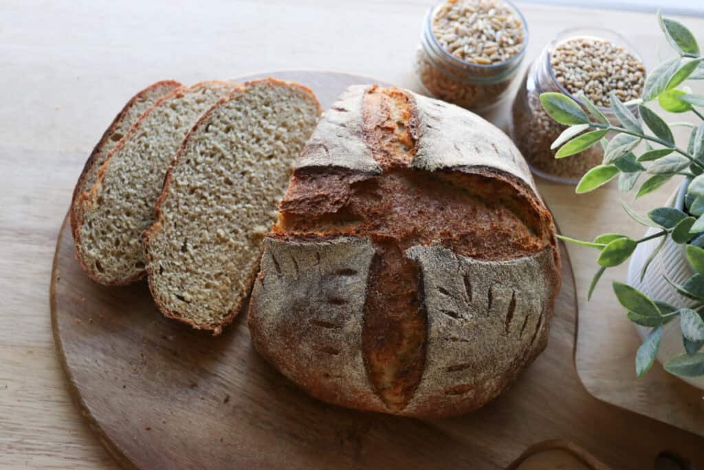 the best fresh milled artisan loaf on a cutting board that has been sliced with grains in jars