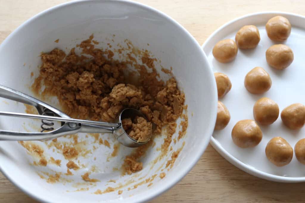 scooping the peanut butter mixture out and rolling into balls on a white plate for the fresh milled buckeye brownie cookies