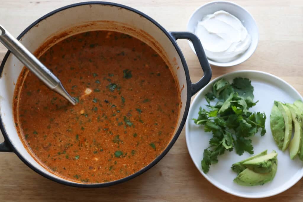 a pot of creamy chicken enchilada soup with a plate of avocados and cilantro