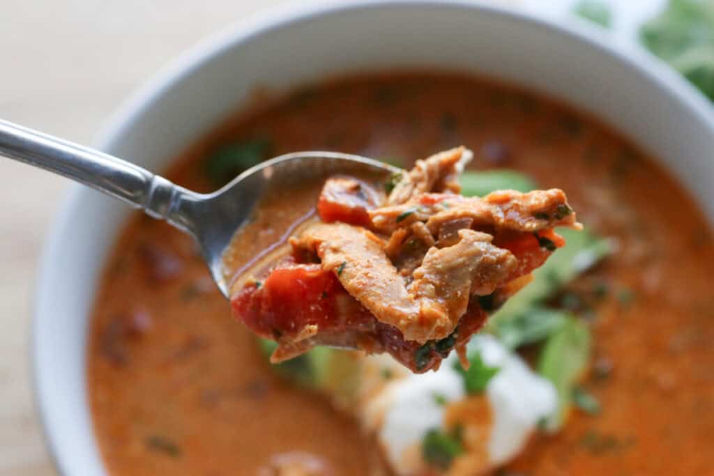 a spoon of creamy chicken enchilada soup over top of a bowl