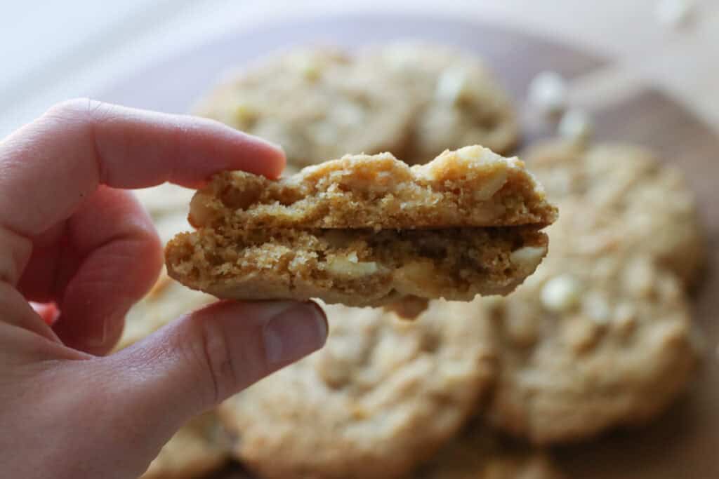 someone holding a Freshly Milled White Chocolate Macadamia Cookie that is broken in half