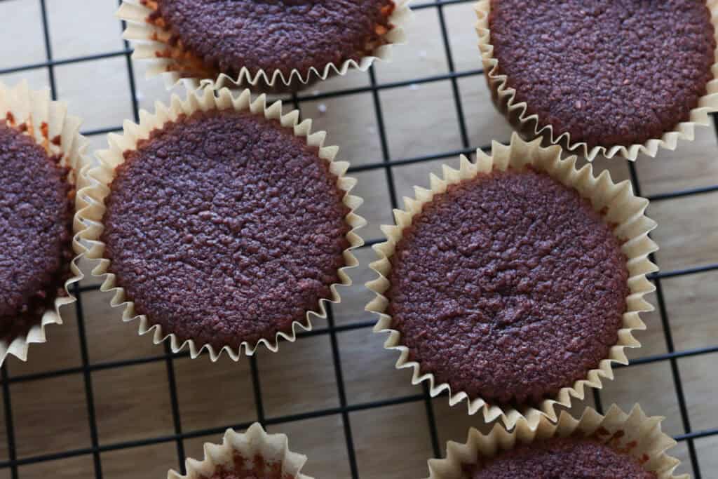 freshly milled red velvet cupcakes in cupcake liners on a black cooling rack