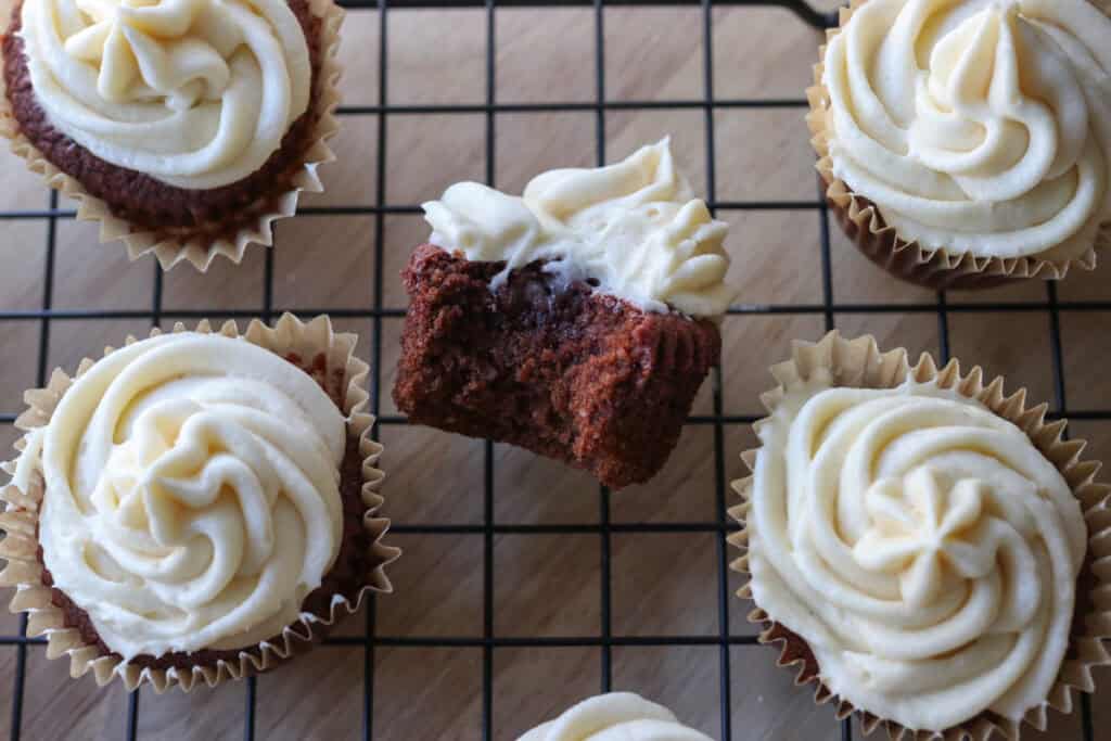 freshly milled red velvet cupcakes on a cooling rack with frosting on top