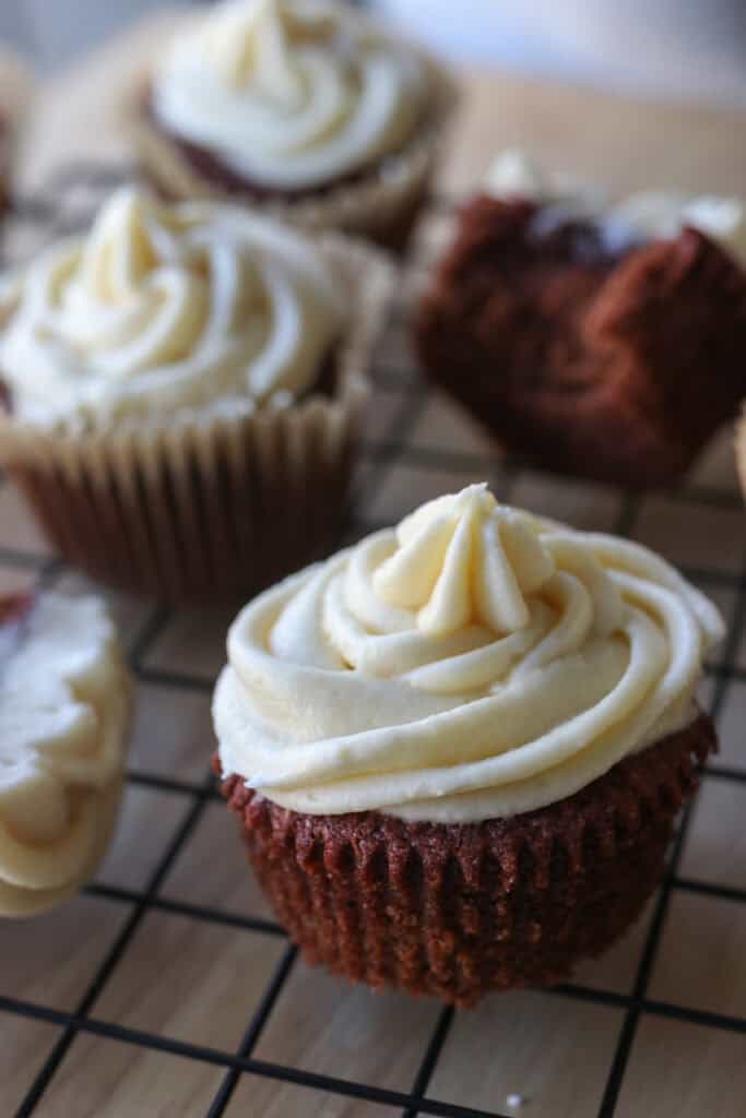 a freshly milled red velvet cupcake with cream cheese frosting on a wire rack
