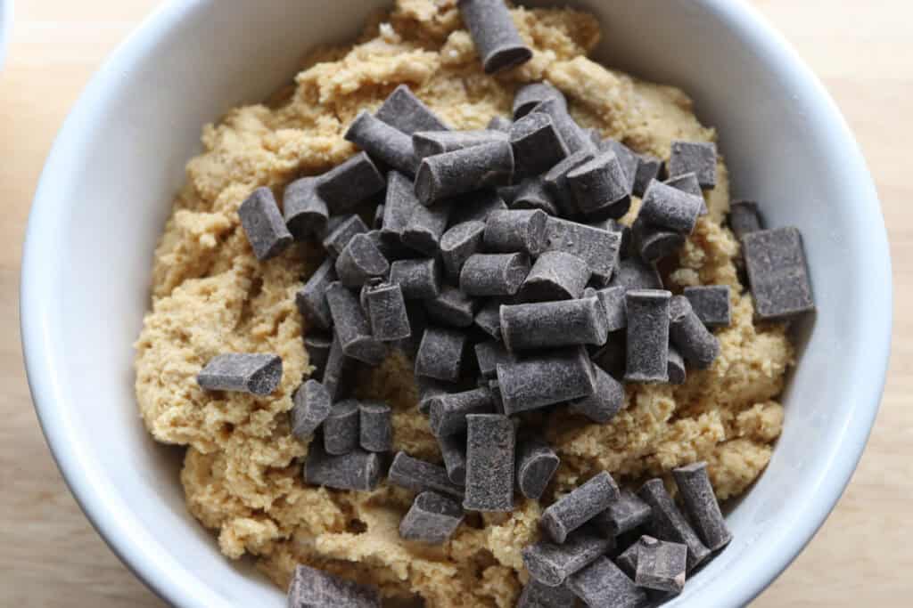chocolate chunks on top of freshly milled chocolate chip biscotti dough in a white bowl