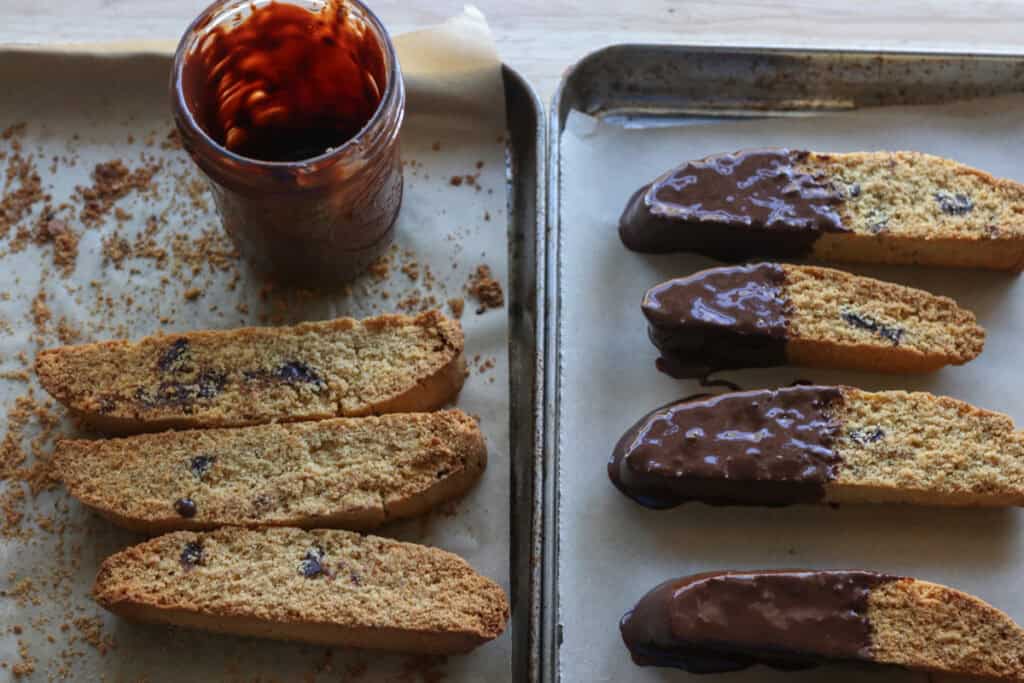 freshly milled chocolate chip biscotti on baking pans being dipped in chocolate