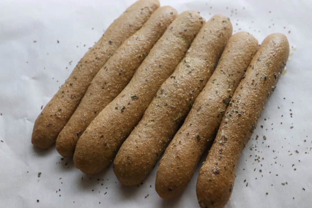 six fresh milled sourdough breadsticks with garlic butter on a piece of white parchment