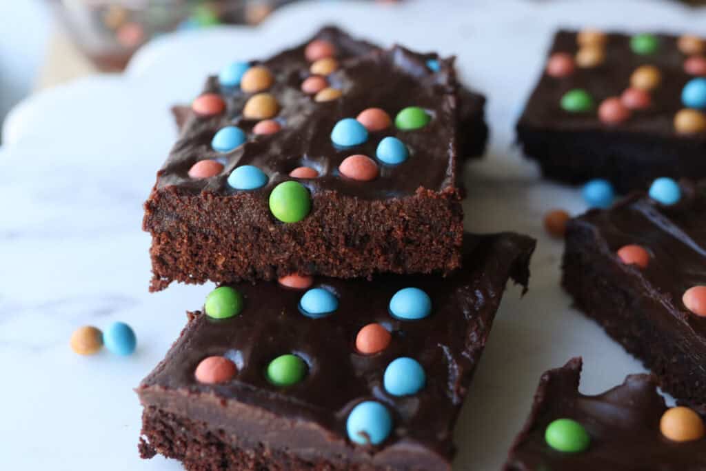 freshly milled fudgy cosmic brownies stacked together with rainbow candy covered chocolate