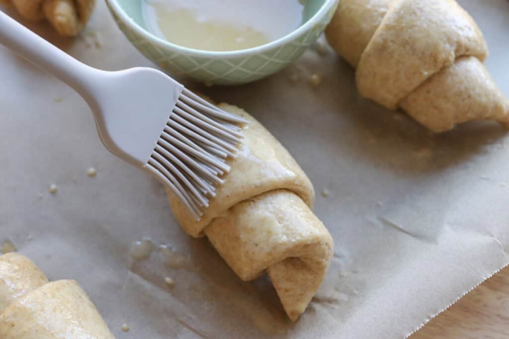 brushing fresh milled flaky buttery croissants with egg wash