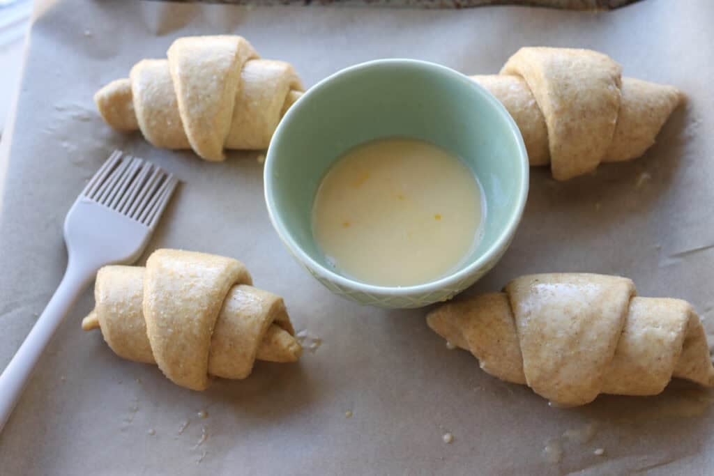 fresh milled flaky buttery croissants on parchment that have been brushed with an egg wash 