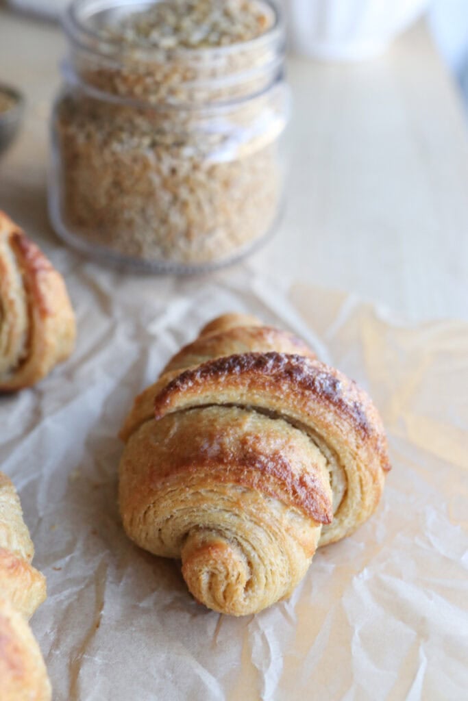 a fresh milled flaky buttery croissant on parchment with a jar of wheat berries behind it