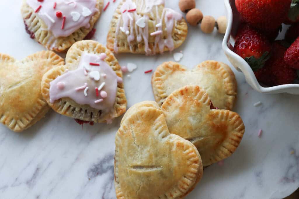 golden brown Fresh Milled Homemade Valentine's Strawberry Poptarts with a slit in the middle of them and a bowl of berries