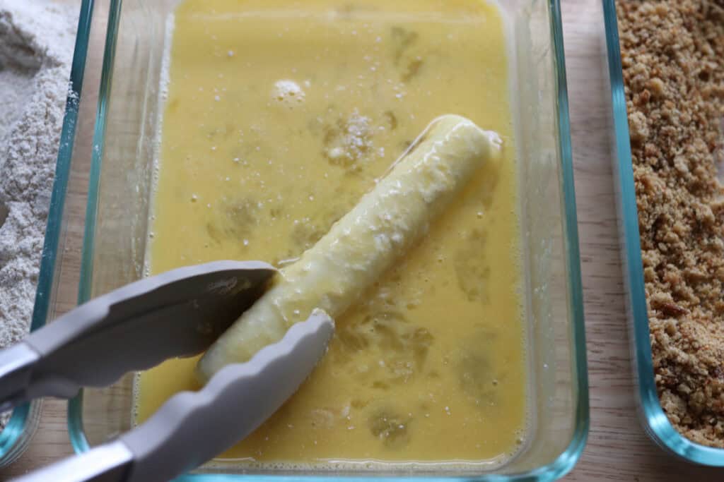 rolling a mozzarella stick in an egg wash
