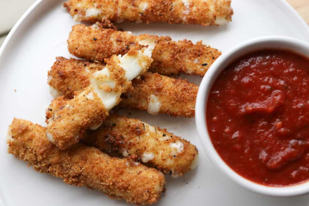 fresh milled fried mozzarella sticks on a plate with marinara sauce