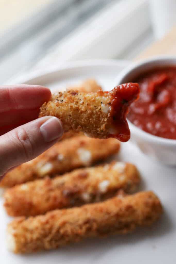 someone holding a fresh milled fried mozzarella stick dipped in marinara sauce