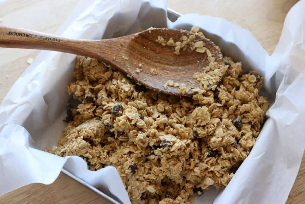 using a wooden spoon to press Easy and Delicious Copycat Heavenly Hunk dough into a square pan